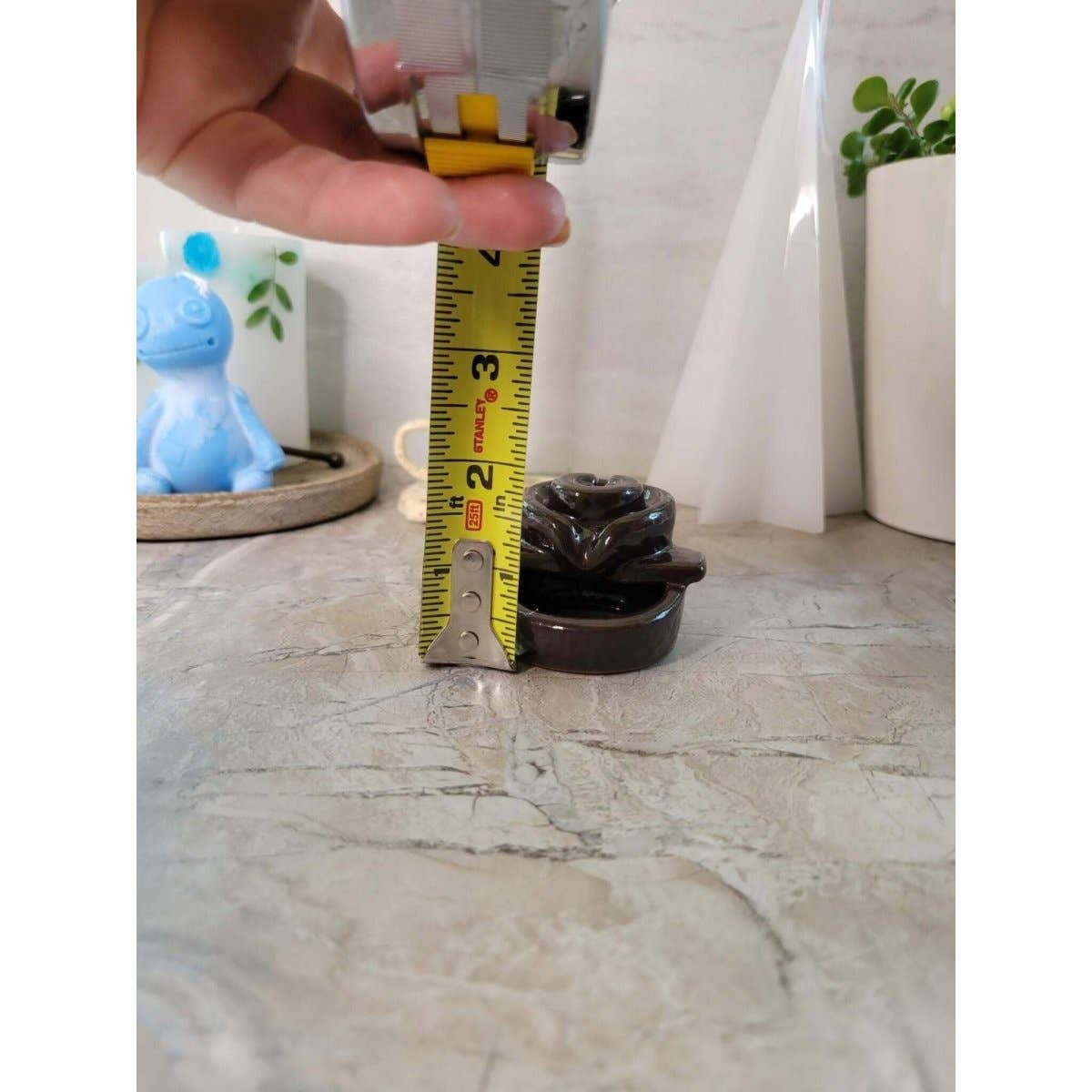 Small brown back flow incense burner  being measured with a tape measure on a marble surface.