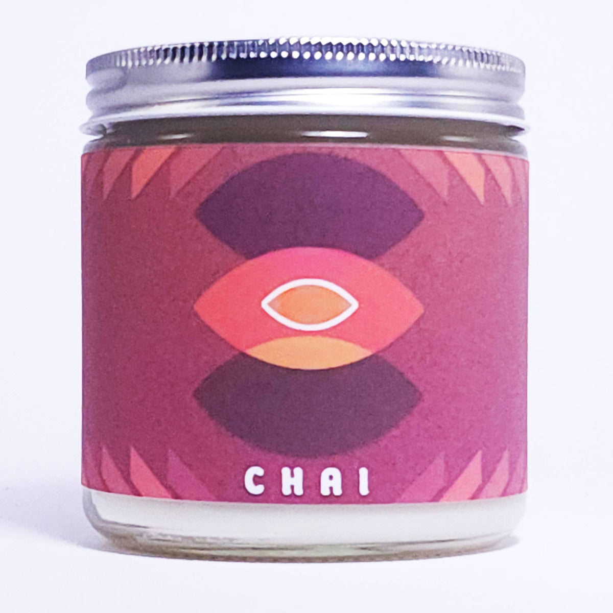 A glass jar candle with a silver metal lid and a pink and purple label featuring a stylized eye design and the word 'CHAI' at the bottom, shown on a white background.