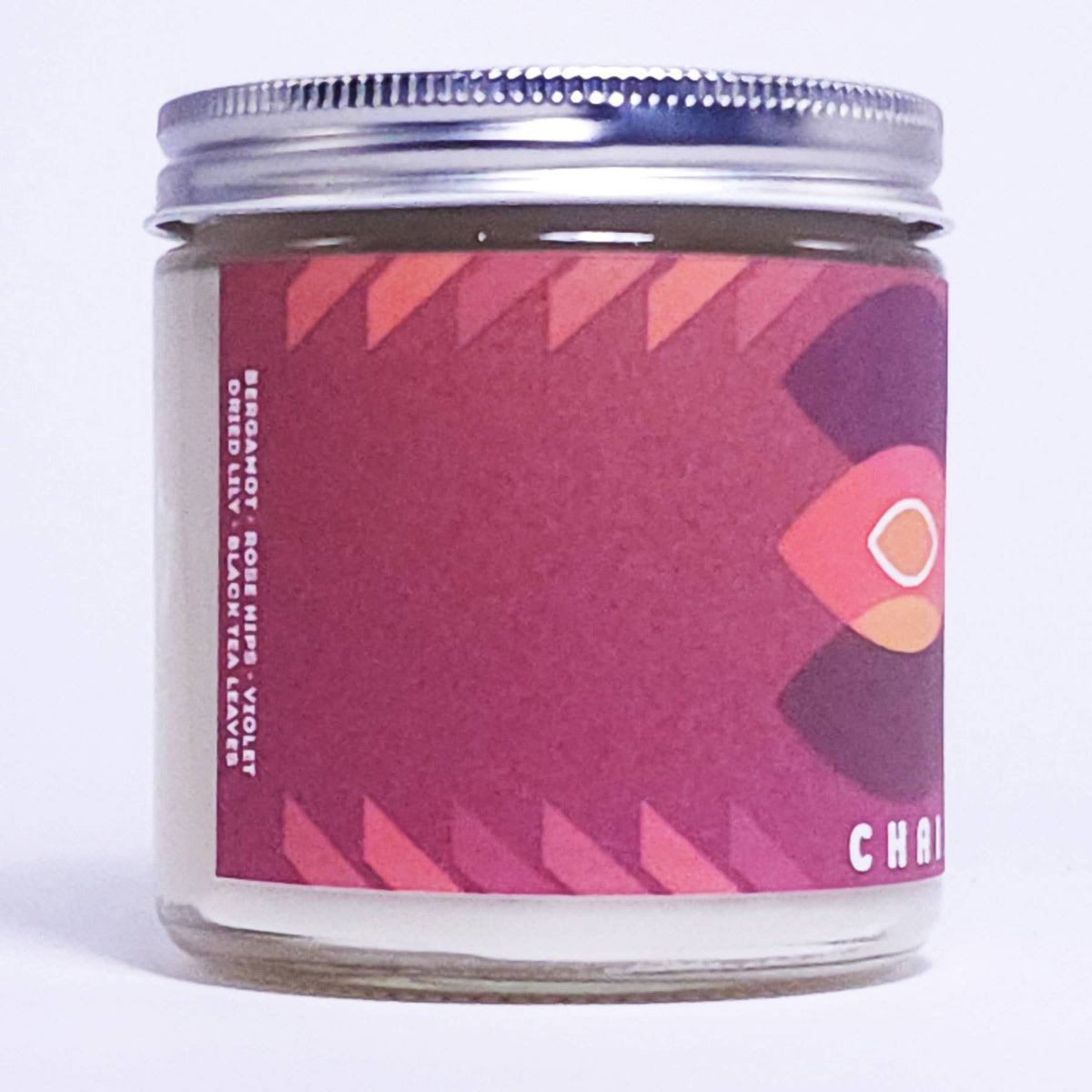 A glass jar candle with a silver metal screw-top lid and a maroon and pink label featuring a stylized bird graphic and the brand name CHAI.