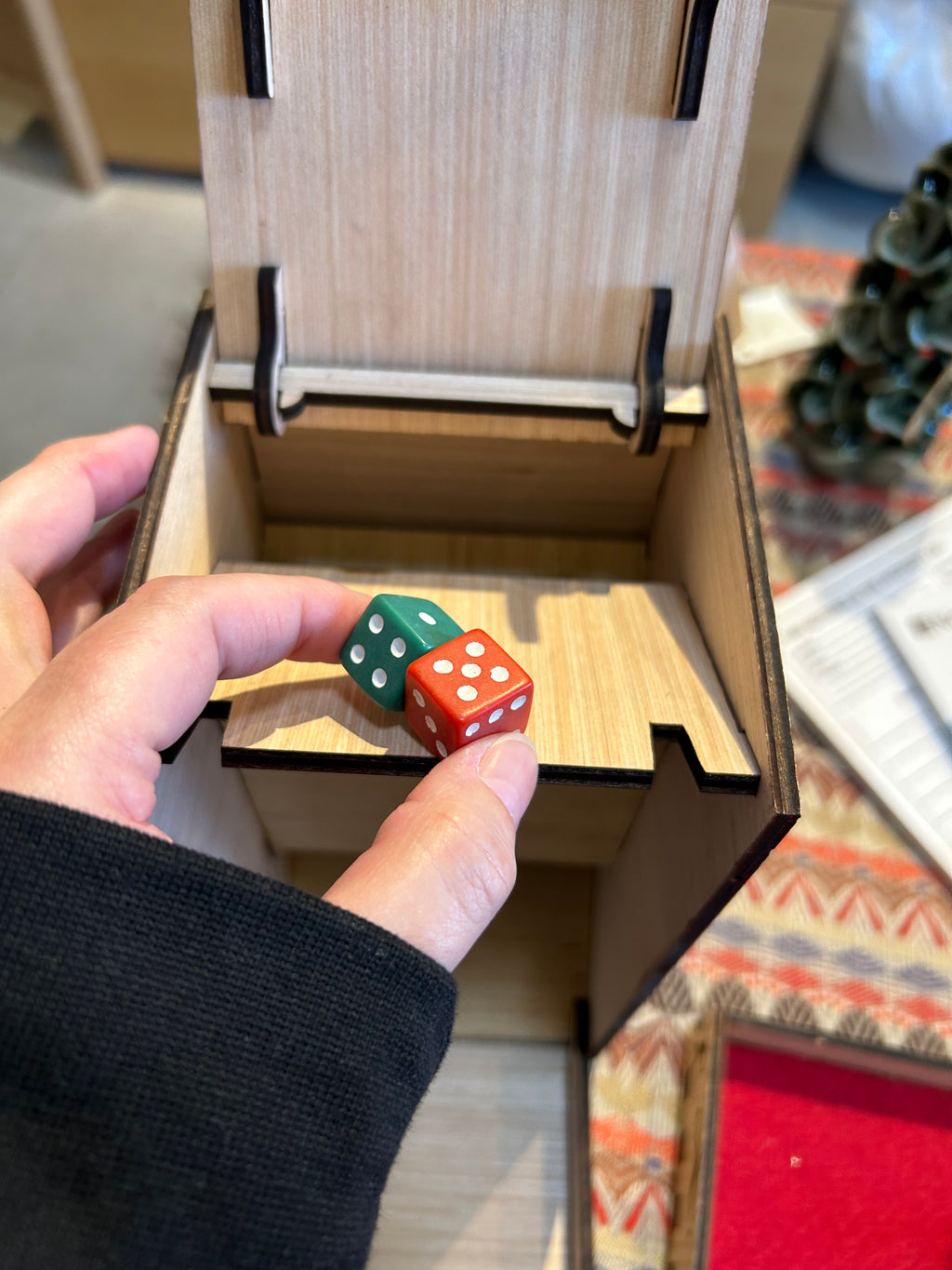 Hand holding two dice in front of a wooden dice tower