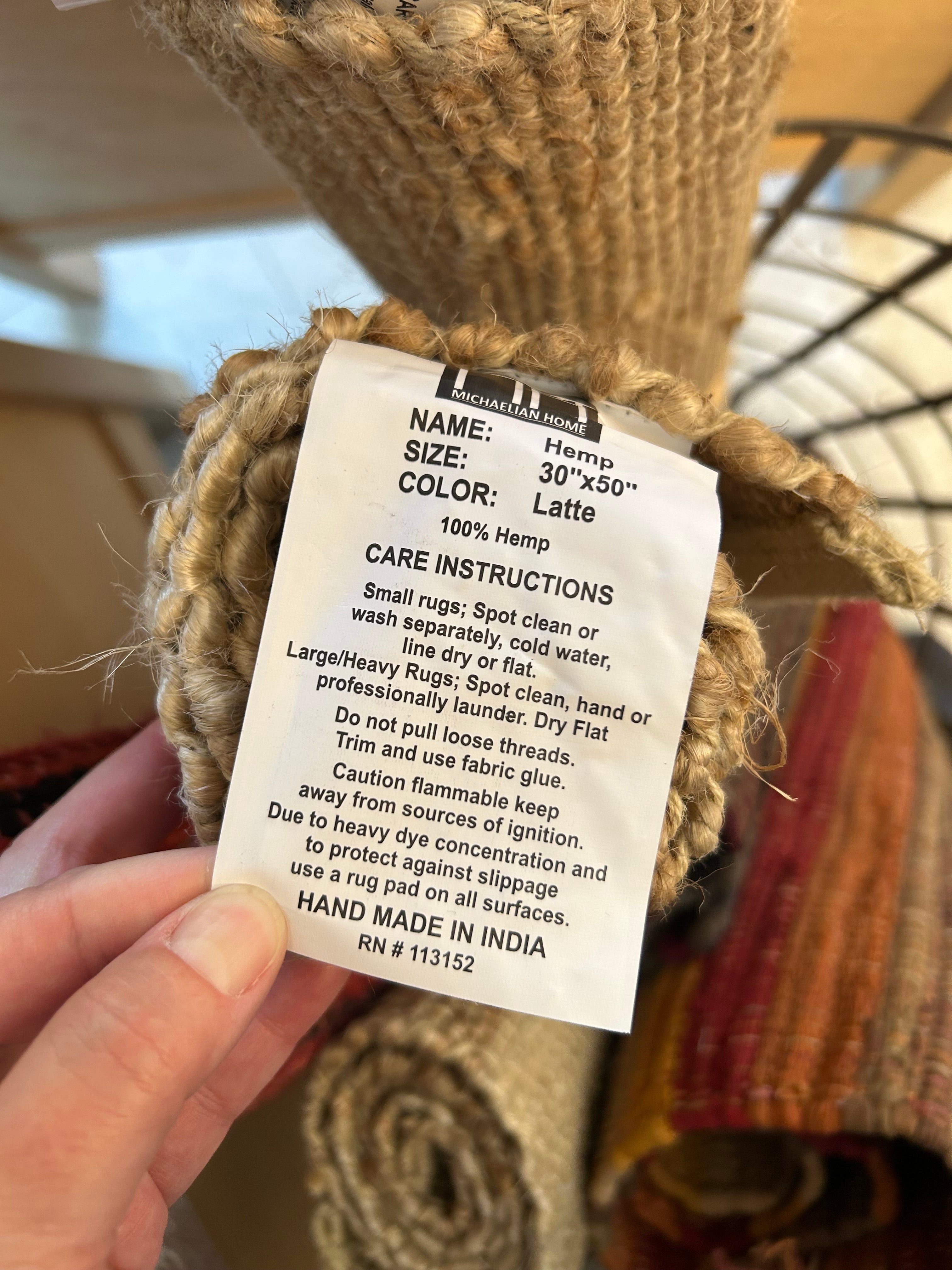 Textile rug with a label held by a hand, showing care instructions and material details.