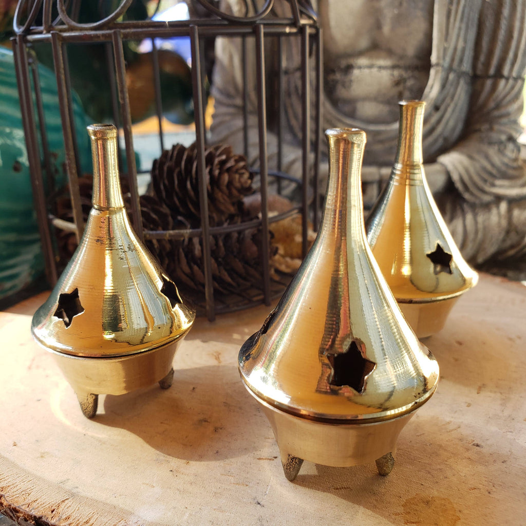Three brass incense burners on a wooden surface with a blurred background