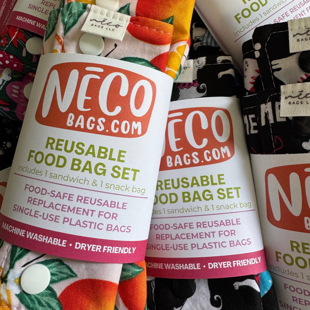 A close-up of a reusable food bag set with printed labels reading 'NICO BAGS.COM REUSABLE FOOD BAG SET' and several colorful fabric bag sections visible behind and around it.