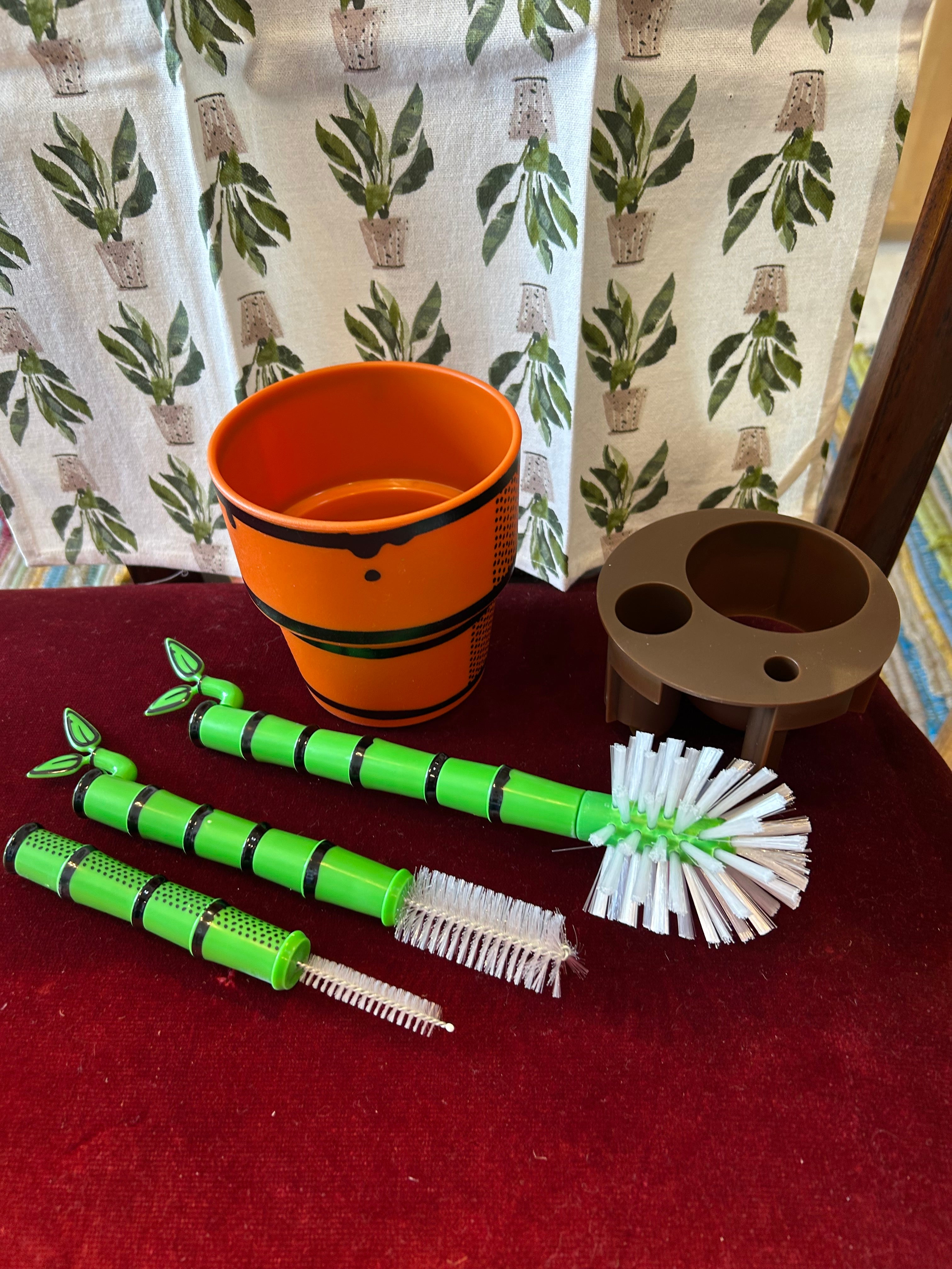 Set of green and white cleaning brushes on a red surface with a Peace Lily Tea Towel by Mahogany background.