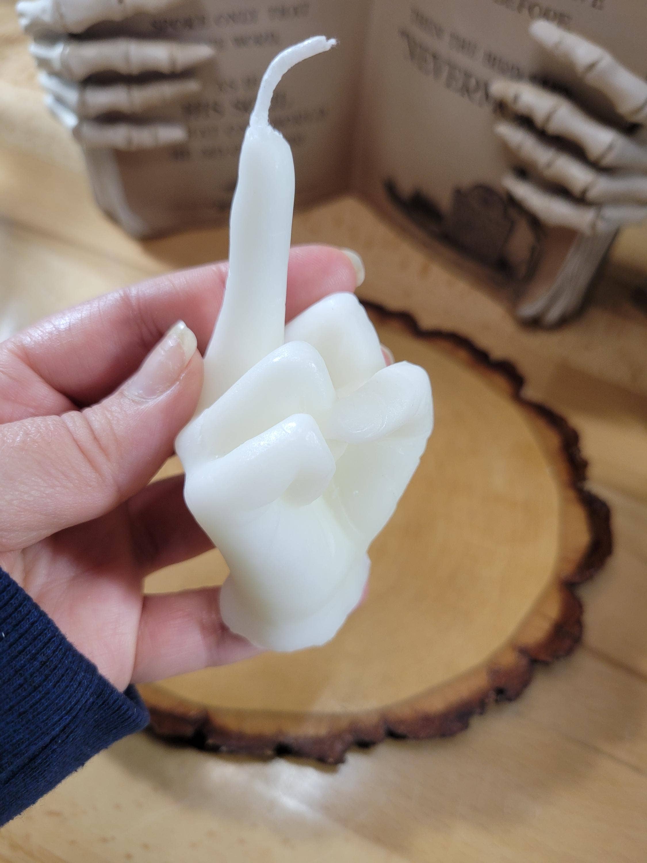 Hand holding a white, abstract candle sculpture on a wooden surface.