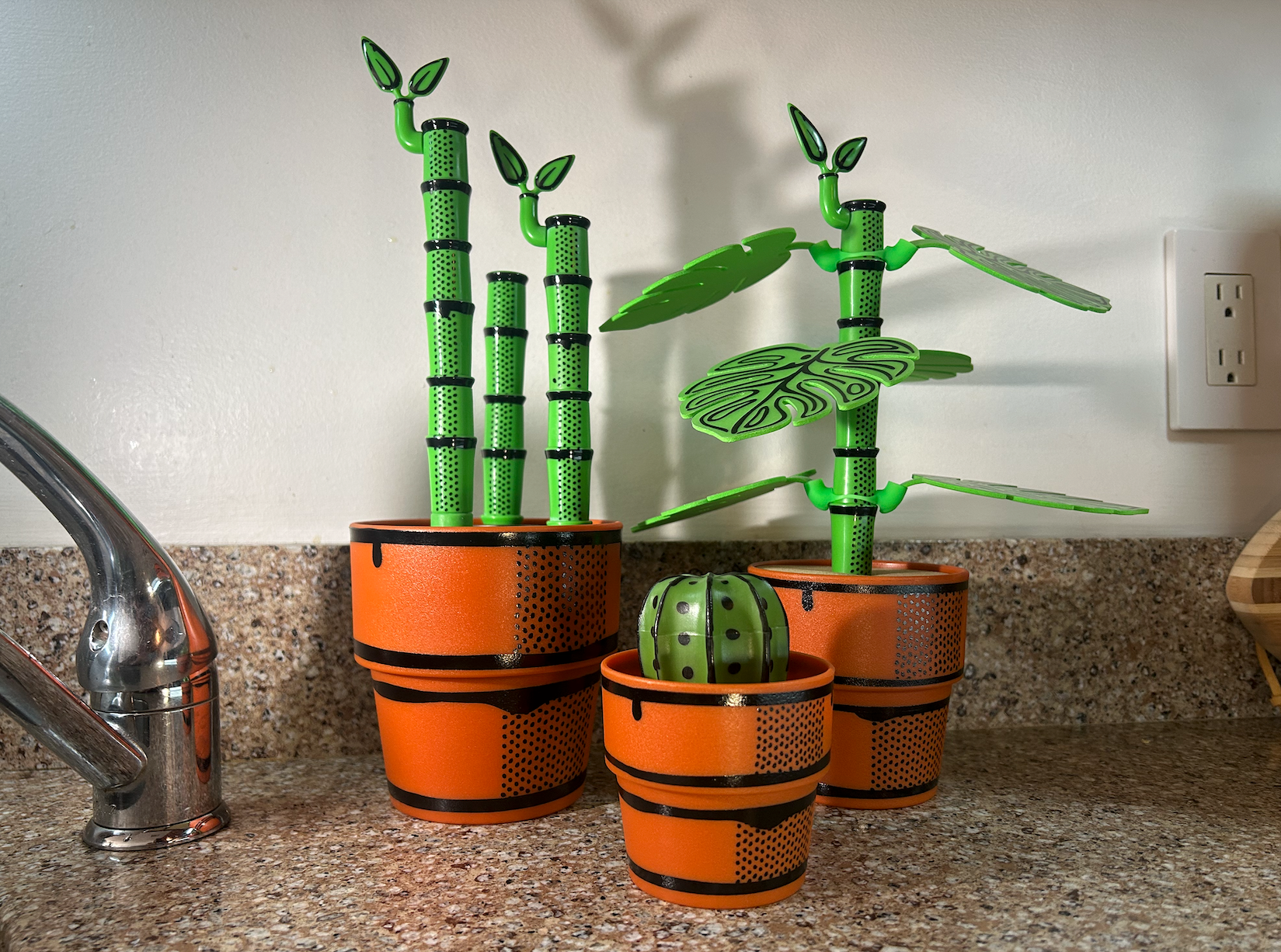 Decorative green plants that are bottle brushes or drink coasters in orange pots on a kitchen counter.