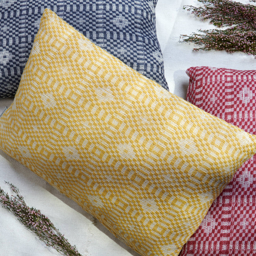 Yellow patterned pillow on a white surface with other pillows in the background