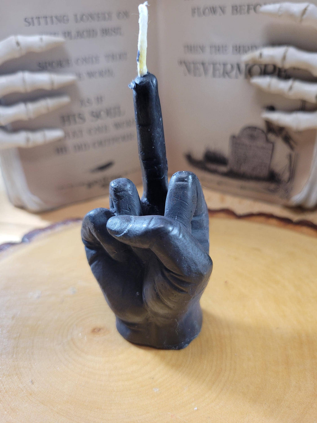 Black candle shaped like a hand holding a lighter on a wooden surface with a blurred background.