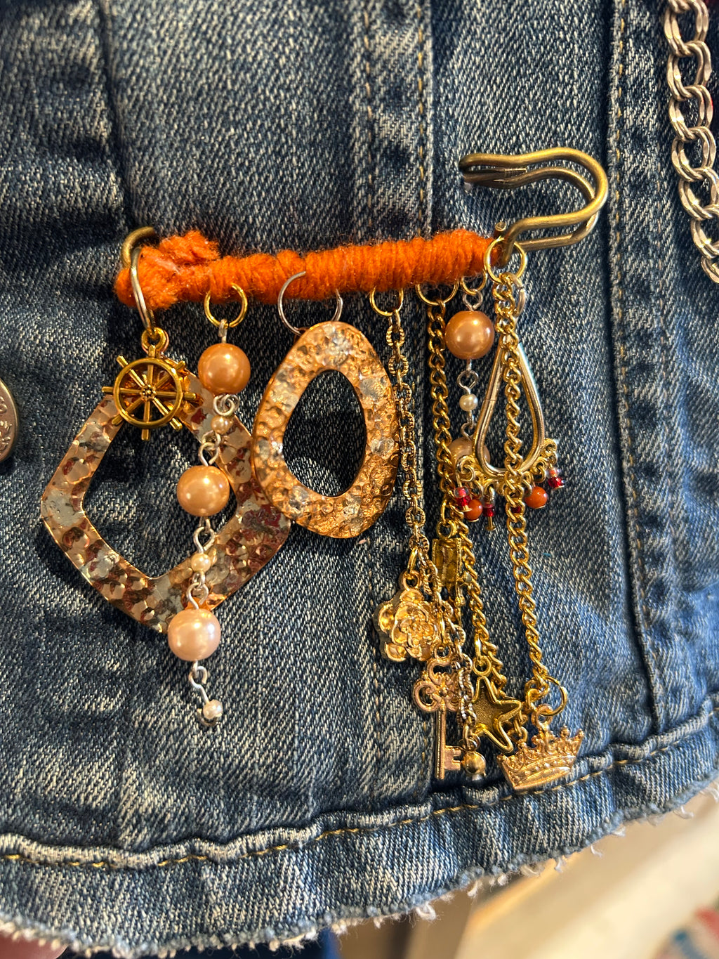 Decorative brooch with chains and beads attached to a denim surface