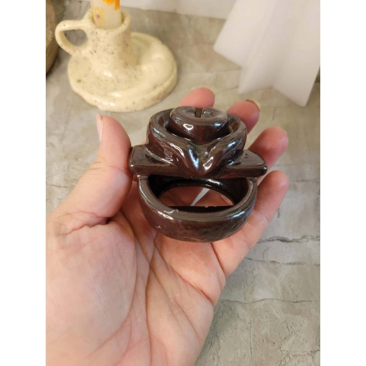Hand holding a small brown ceramic back flow incense burner with a blurred background