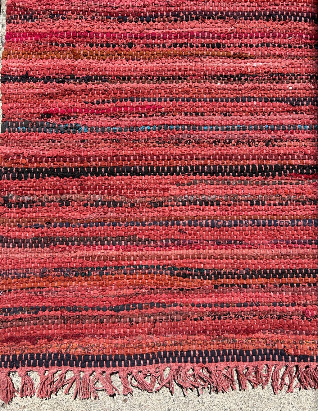 Close-up of a textured red and black rug with fringes.