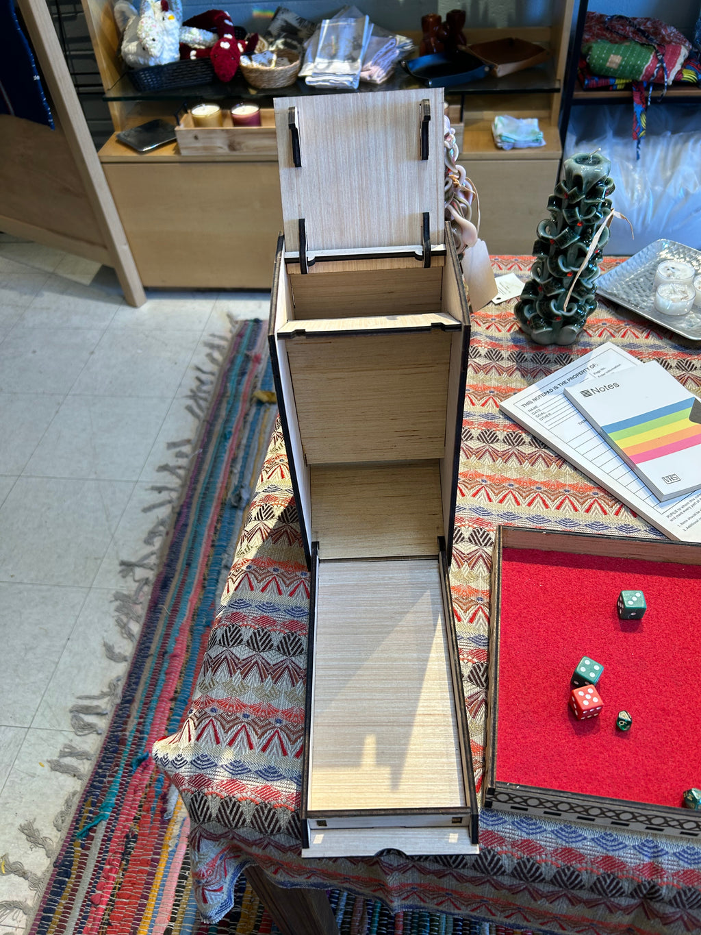 Open wooden dice tower with shelves in background against a colorful patterned rug.