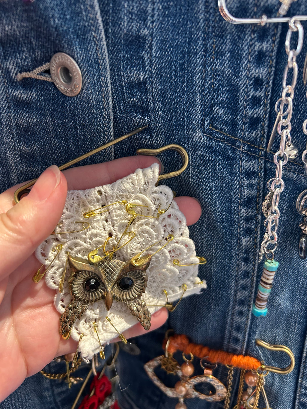 Hand holding a decorative brooch with intricate design against a denim background