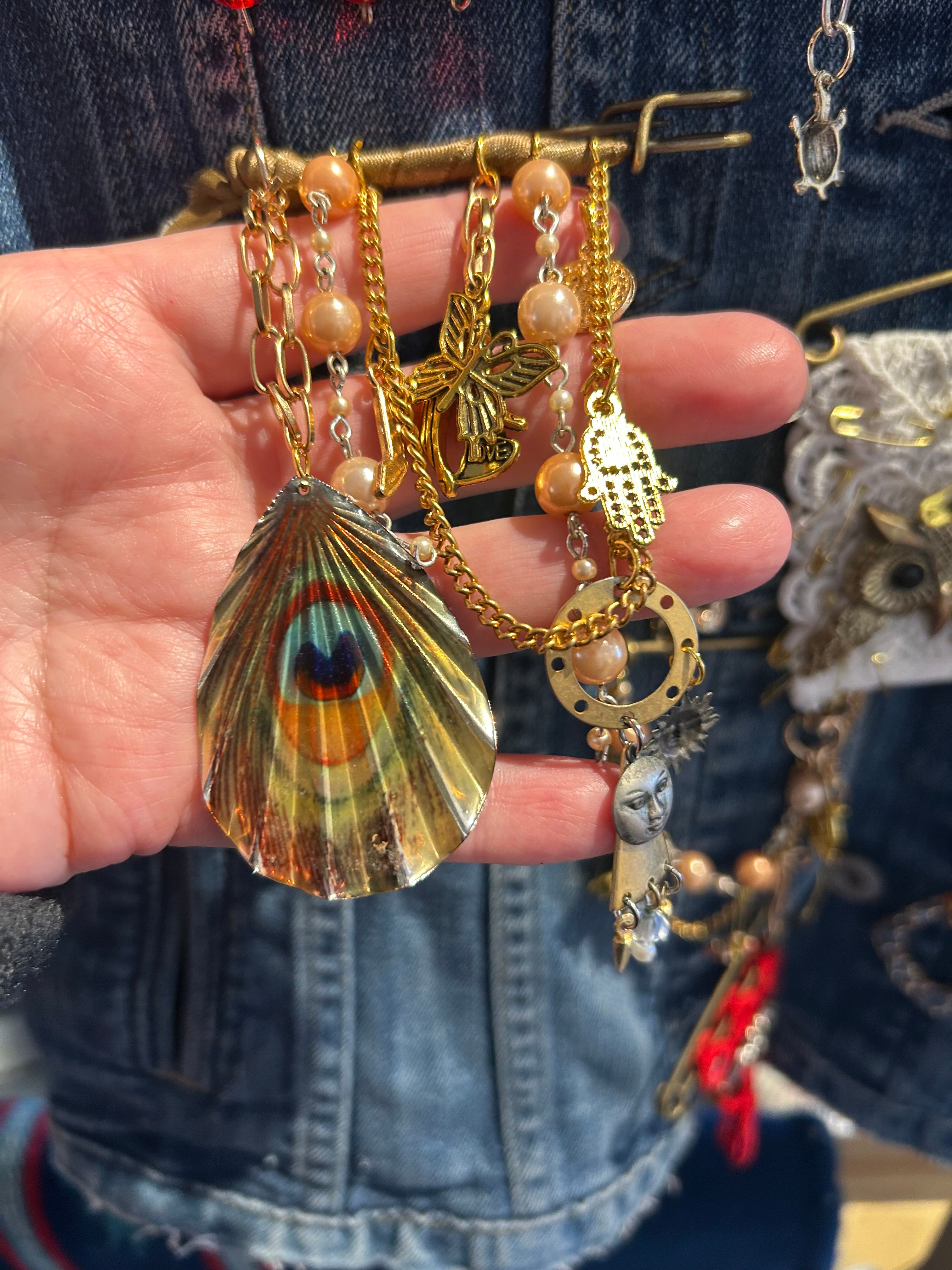 Hand holding a colorful peacock feather charm bracelet with various other charms.