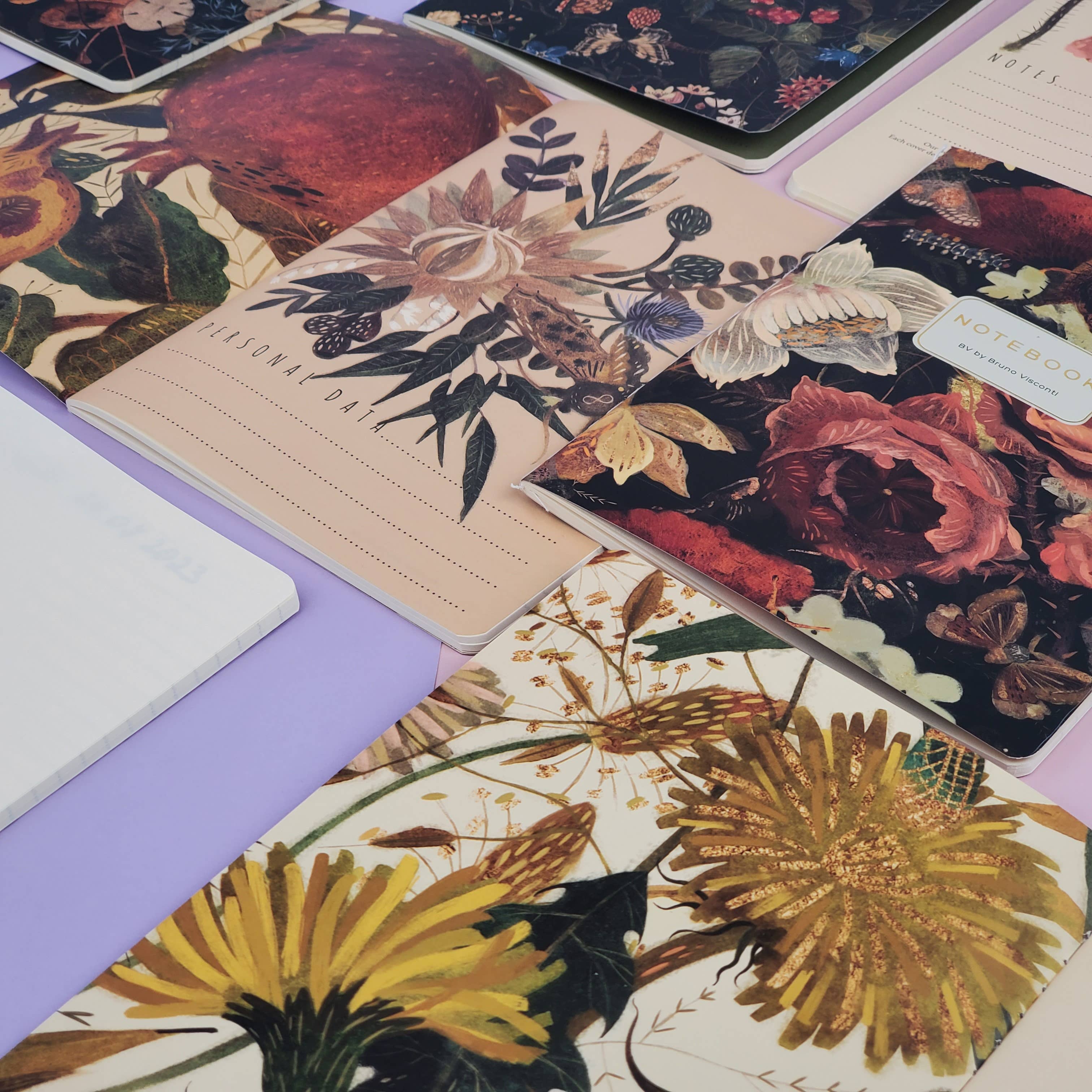 Collection of floral notebooks and stationery items on a purple surface