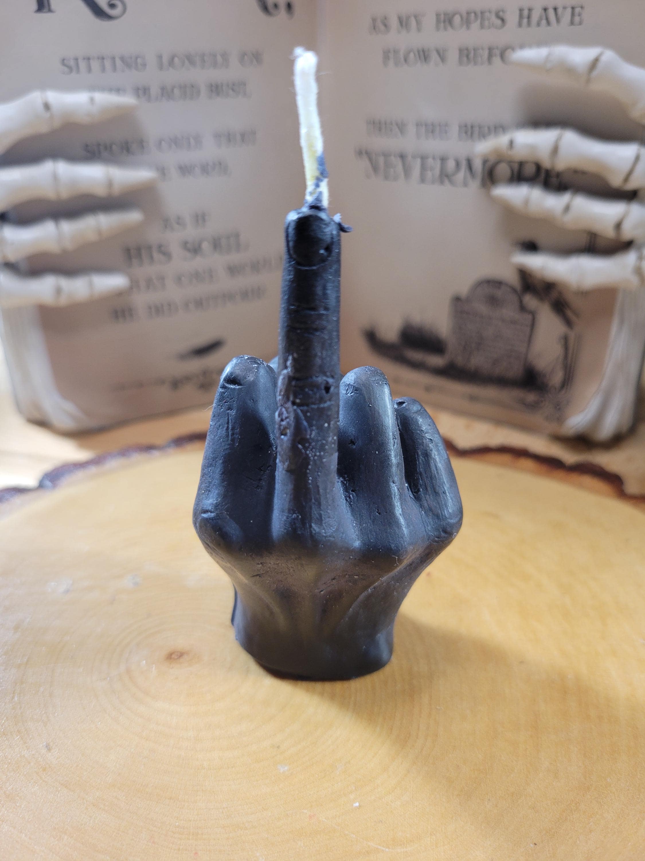 Black hand-shaped candle with a lit wick on a wooden surface.