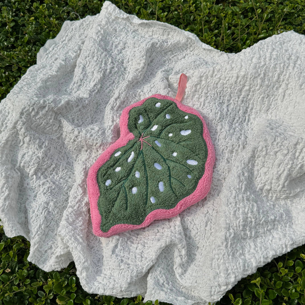 Green leaf-shaped hand towel with pink border on a textured white surface