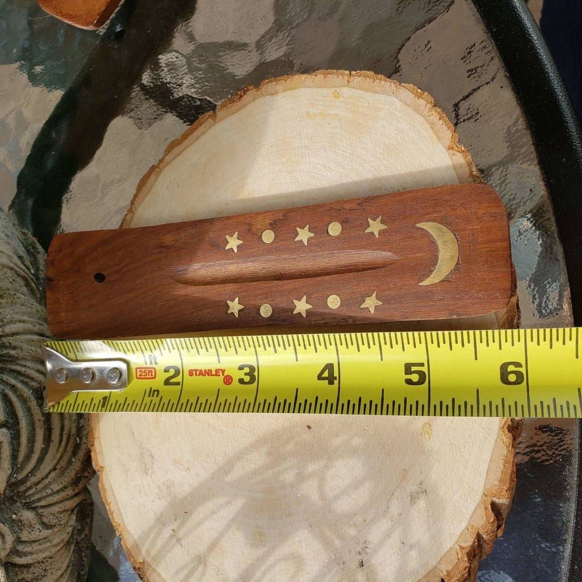 Wooden tool with star and moon designs on a tree stump with a Stanley tape measure for scale.