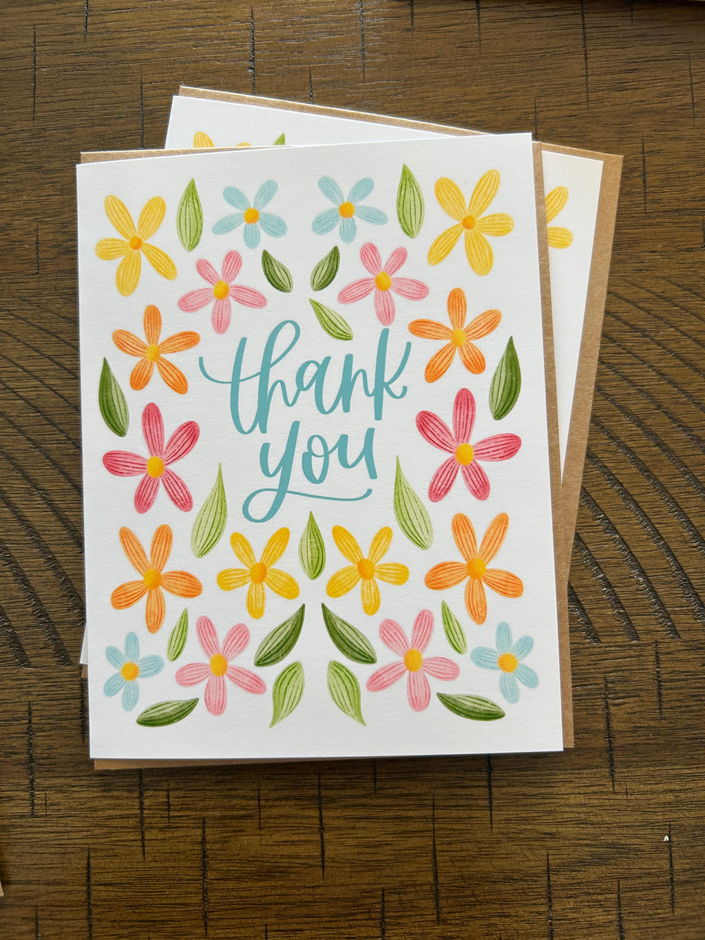 Greeting card with colorful flowers and 'thank you' text on a wooden surface