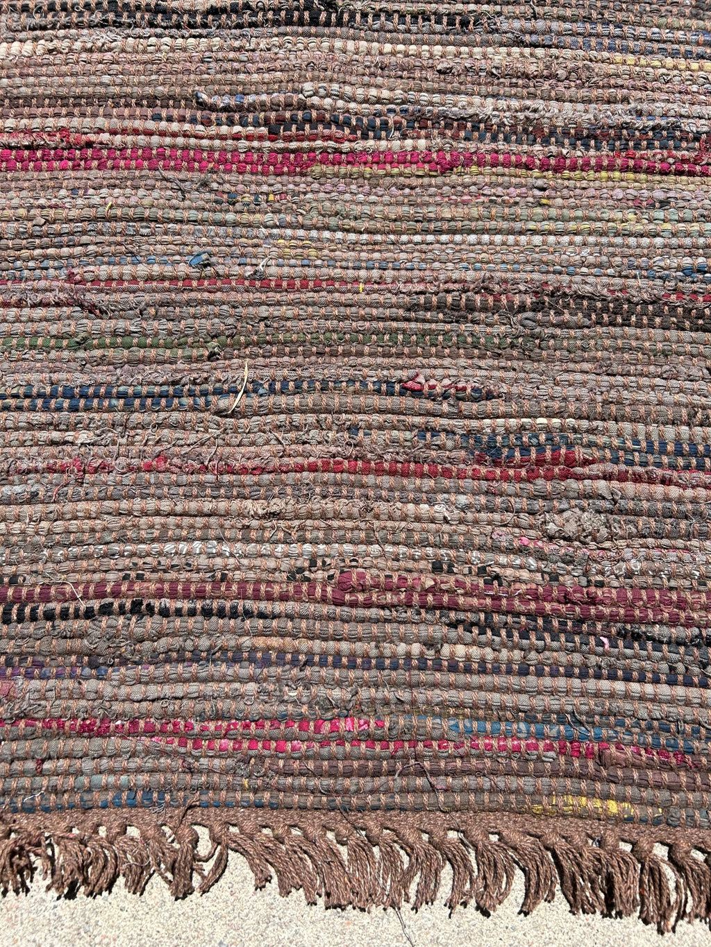 Close-up of a textured rug with multicolored stripes and fringes.