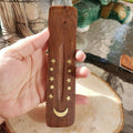 Wooden incense stick holder with star and moon designs held by a hand.