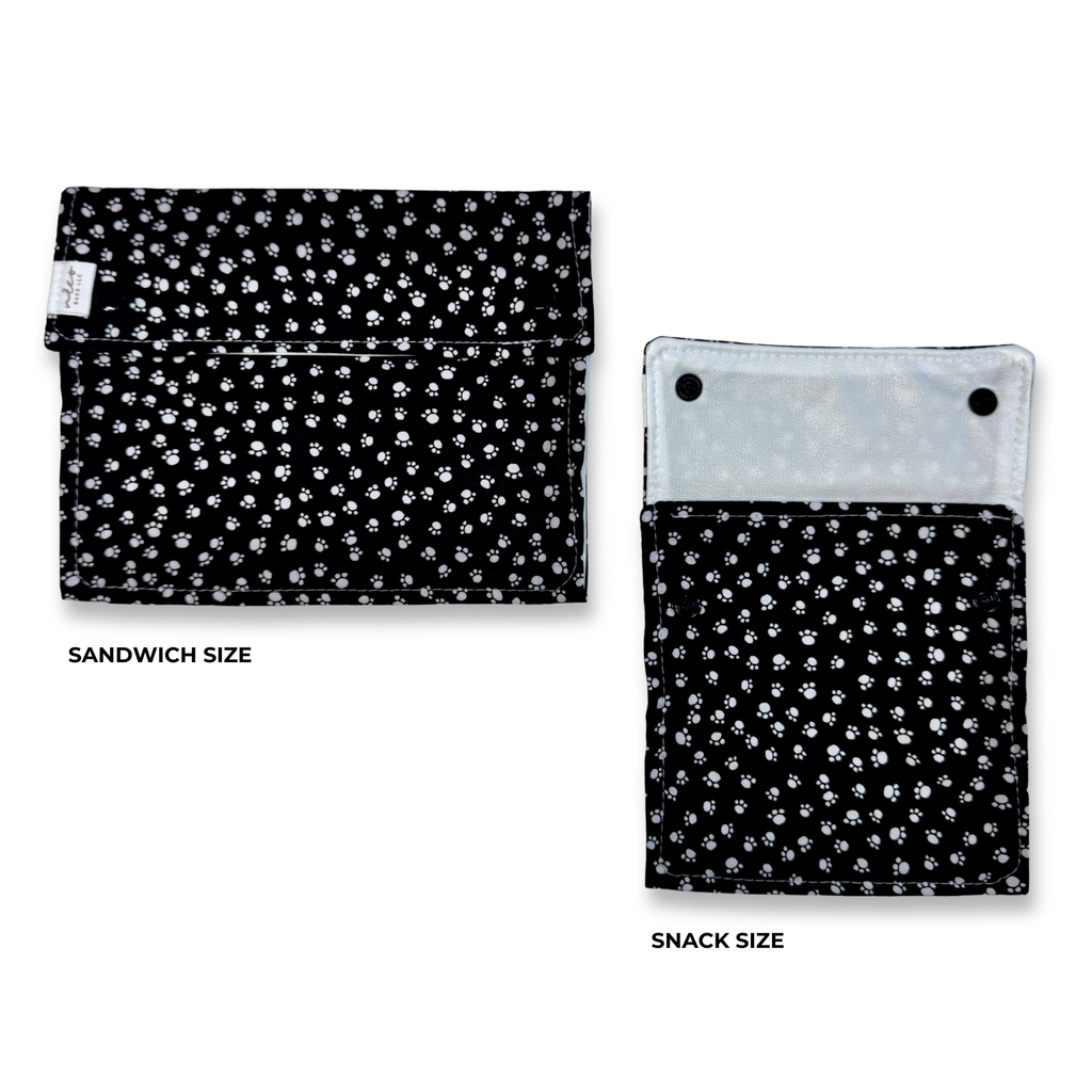 Two fabric pouches shown on a white background, labeled SANDWICH SIZE and SNACK SIZE. Both have a black background with a small white confetti and paws pattern and a light gray inner lining visible on the right pouch.