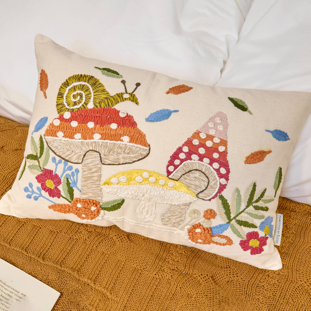 Decorative pillow with embroidered mushrooms and snail on a textured surface