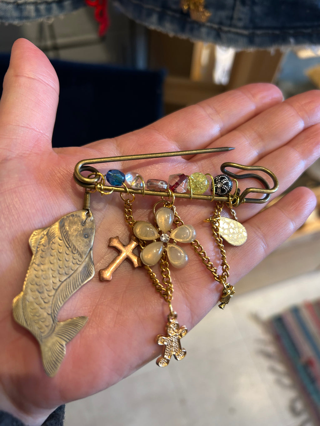 Hand holding various gold jewelry pieces including a safety pin, fish charm, and cross.