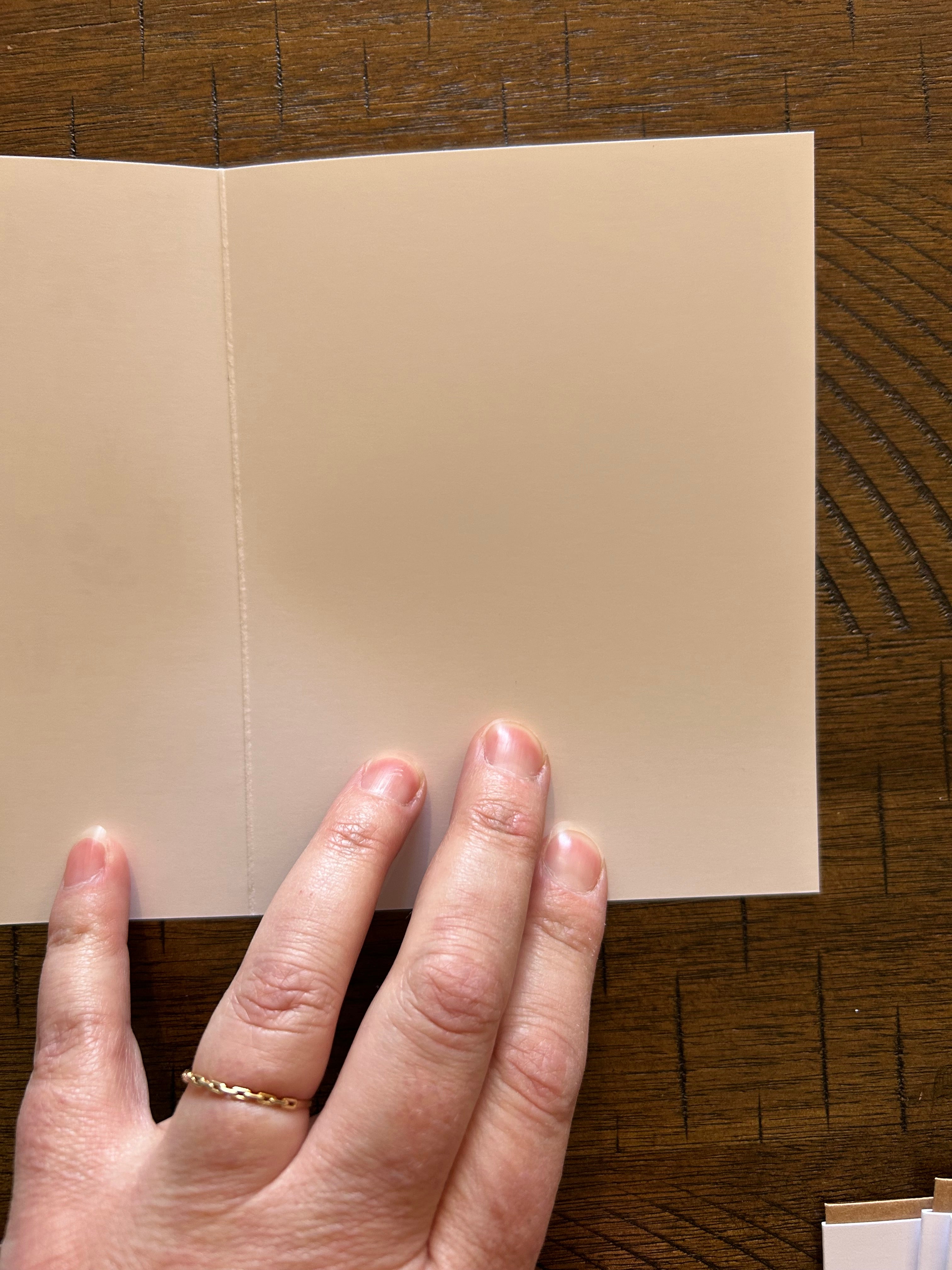 Hand holding a greeting card showing blank white inside on a wooden surface