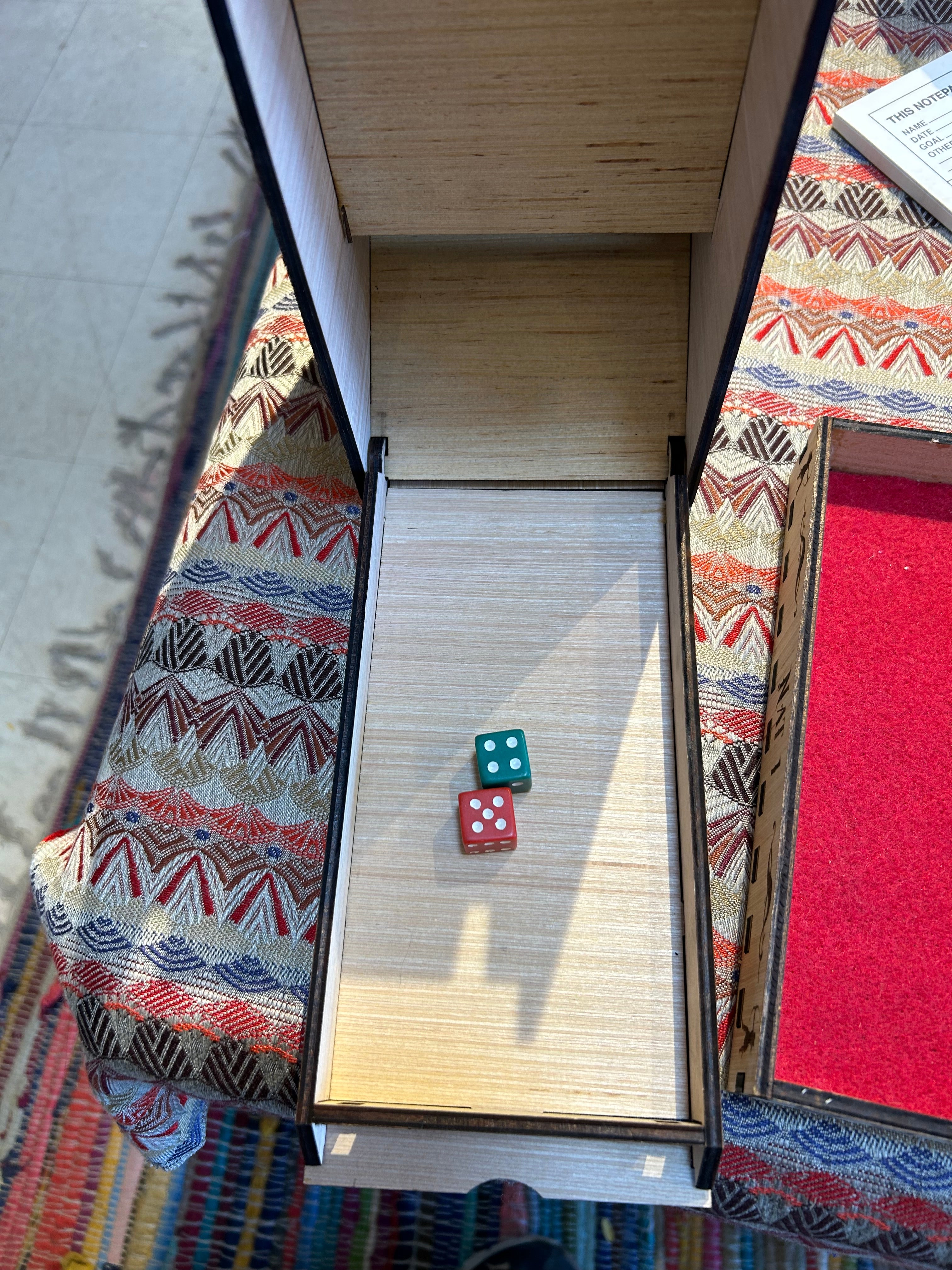 Two dice on a dice tower tray on a  surface with a patterned fabric and wooden furniture in the background.