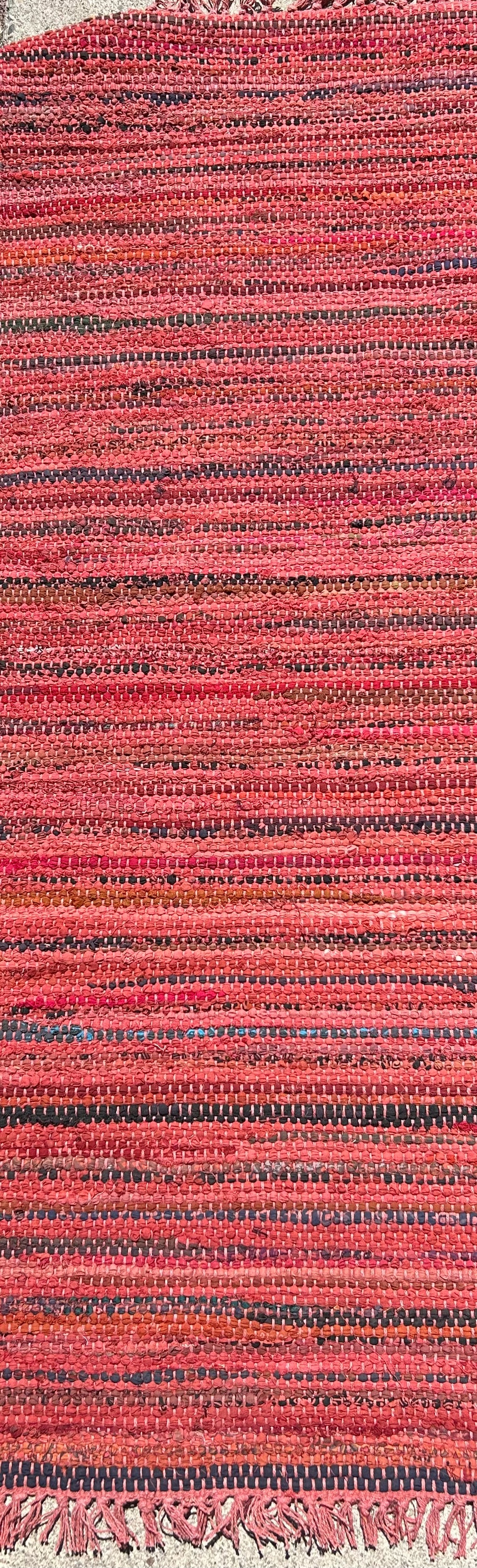 Close-up of a textured red and black woven rug with tassels.