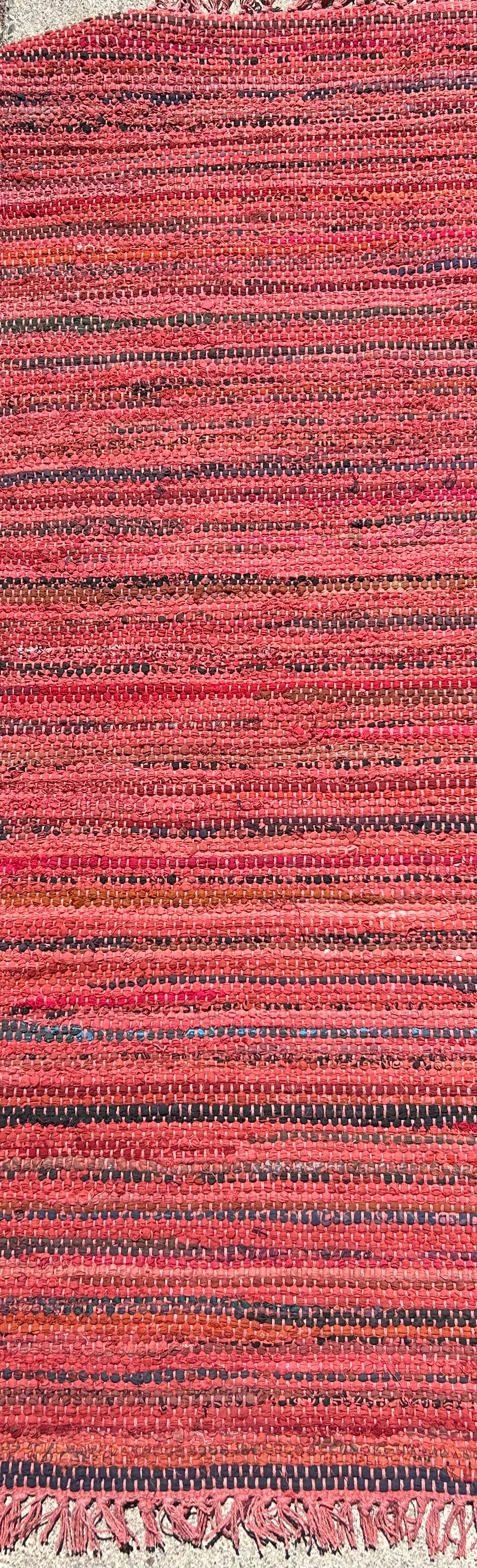 Close-up of a textured red and black woven rug with tassels.