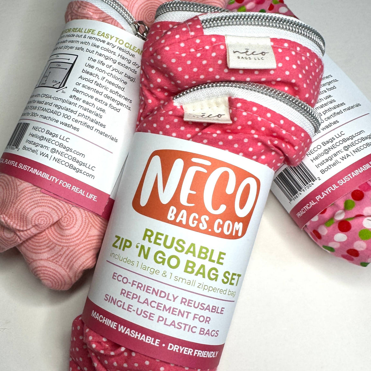 Three reusable zippered go bags from NECO BAGS.COM arranged on a white surface, with the center bag prominently showing a pink and white polka dot pattern and the brand label.