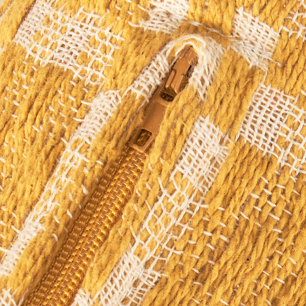 Close-up of a gold zipper on a textured yellow and white fabric background