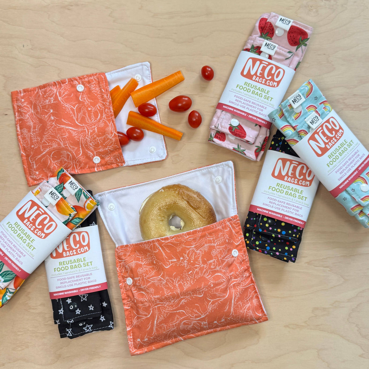 A flat-lay of Neco Backpack reusable food bar sets on a light wood surface, featuring various colorful fabric pouches and snack packaging.
