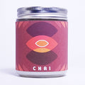 A glass jar candle with a silver metal lid and a textured pinkish-red label featuring a stylized eye design and the word 'CHAI' at the bottom, set against a plain white background.