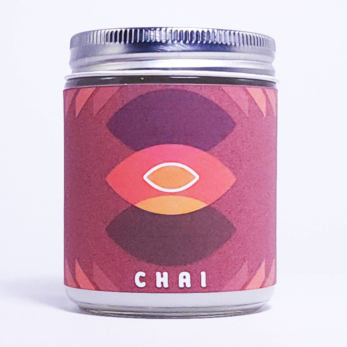 A glass jar candle with a silver metal lid and a textured pinkish-red label featuring a stylized eye design and the word 'CHAI' at the bottom, set against a plain white background.