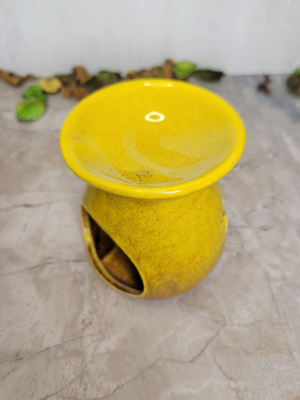 Yellow ceramic oil burner on a textured surface with a blurred background