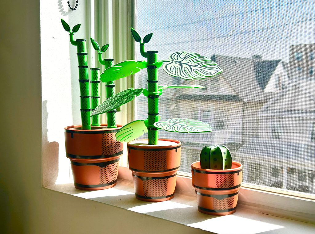 Decorative potted plants that are bottle brushes or drink coasters on a windowsill with a view of houses outside.