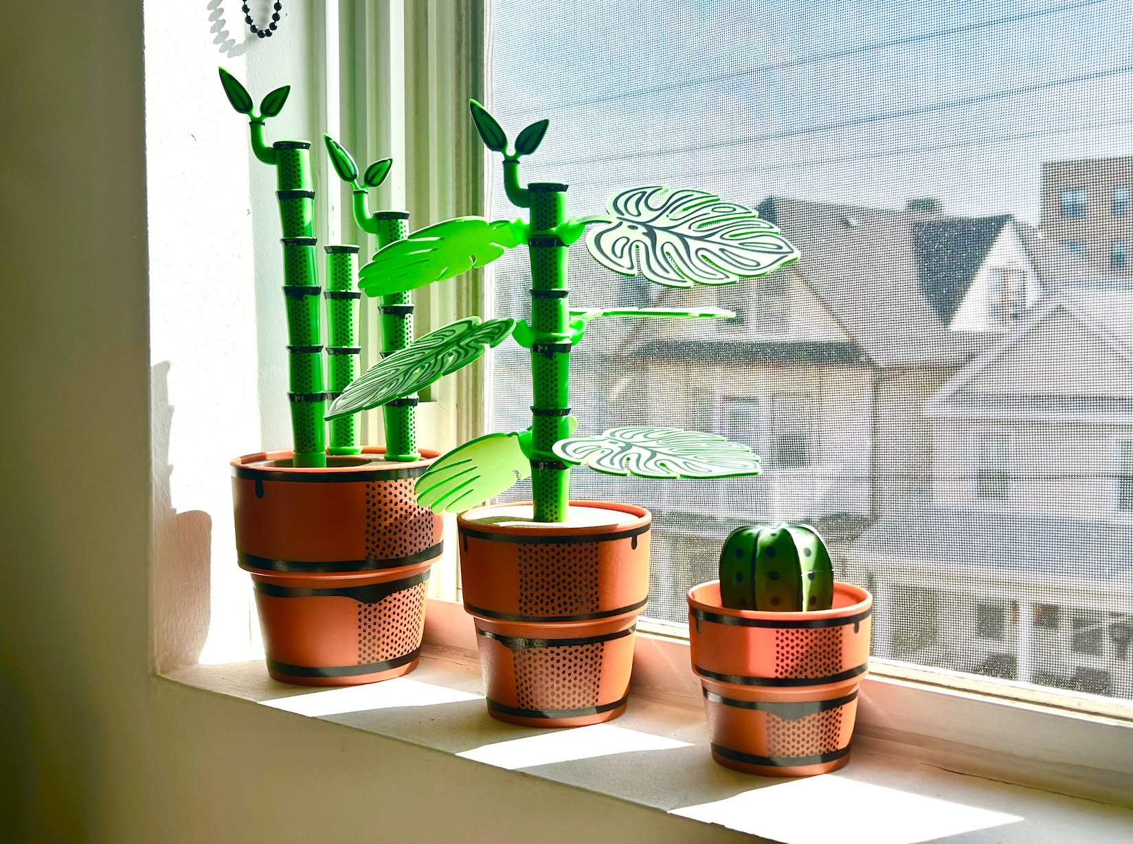 Decorative potted plants that are bottle brushes or drink coasters on a windowsill with a view of houses outside.