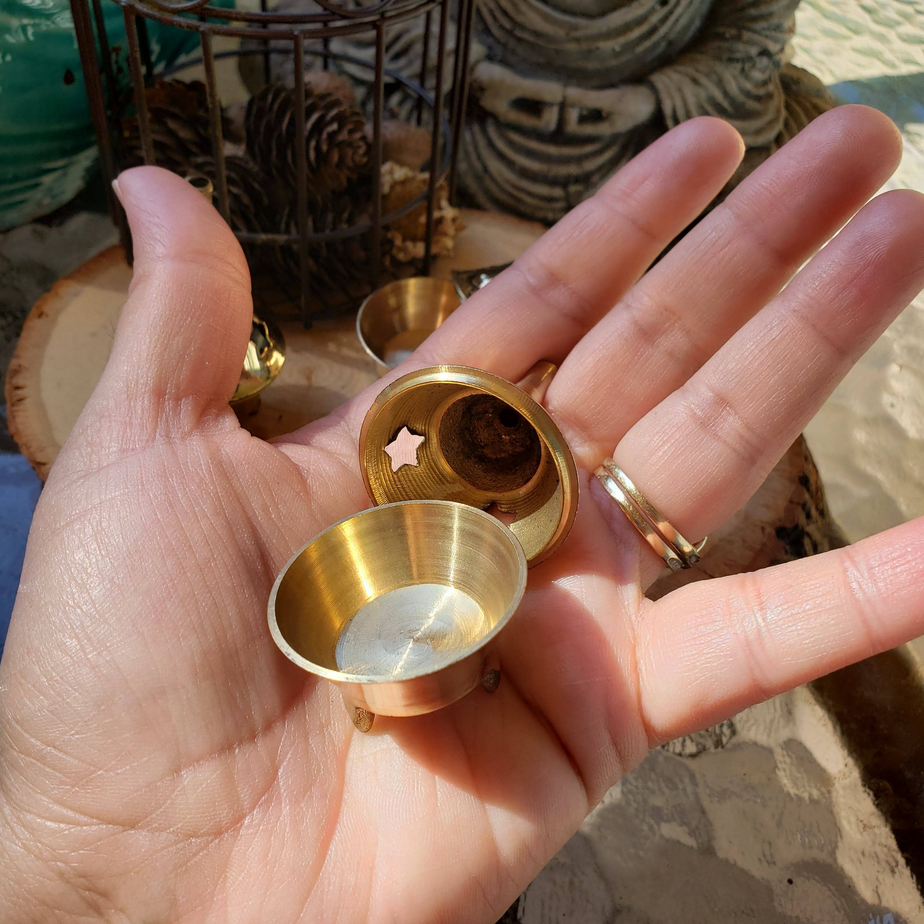 Hand holding a small brass incense holder with a star design on a blurred background