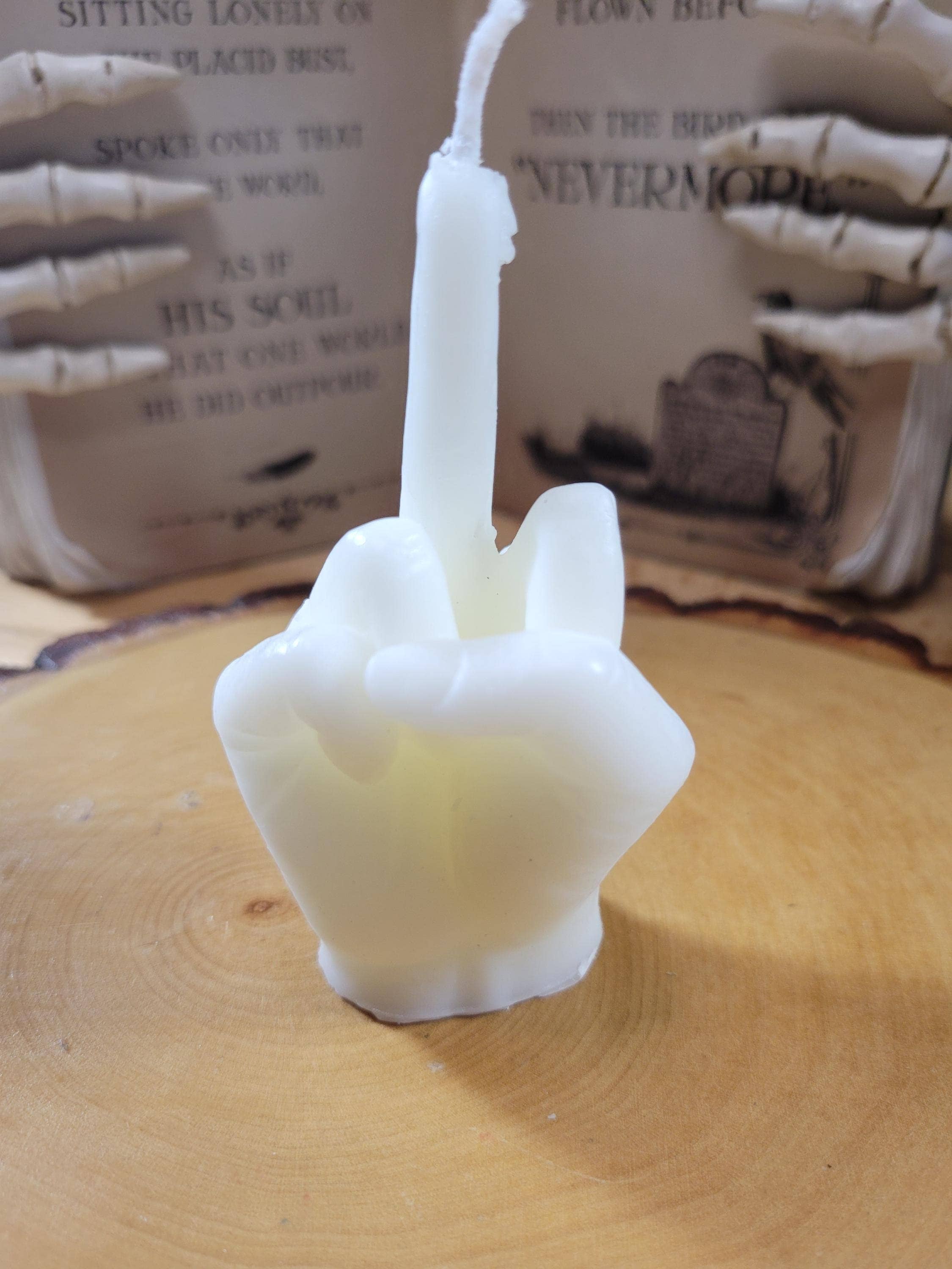 White candle shaped like a hand making a peace sign on a wooden surface with a blurred background.