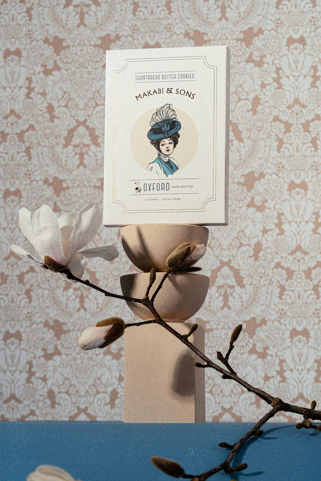 COokie package with a woman's portrait and text, placed on a floral arrangement against a patterned wall.