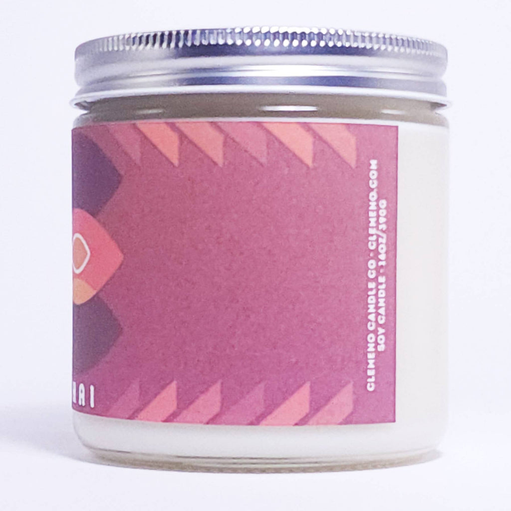 A glass jar candle with white wax and a silver metal lid, featuring a pink and purple geometric label. The label includes white text reading 'CLESHING CANDLE CO - CLIFENCO.