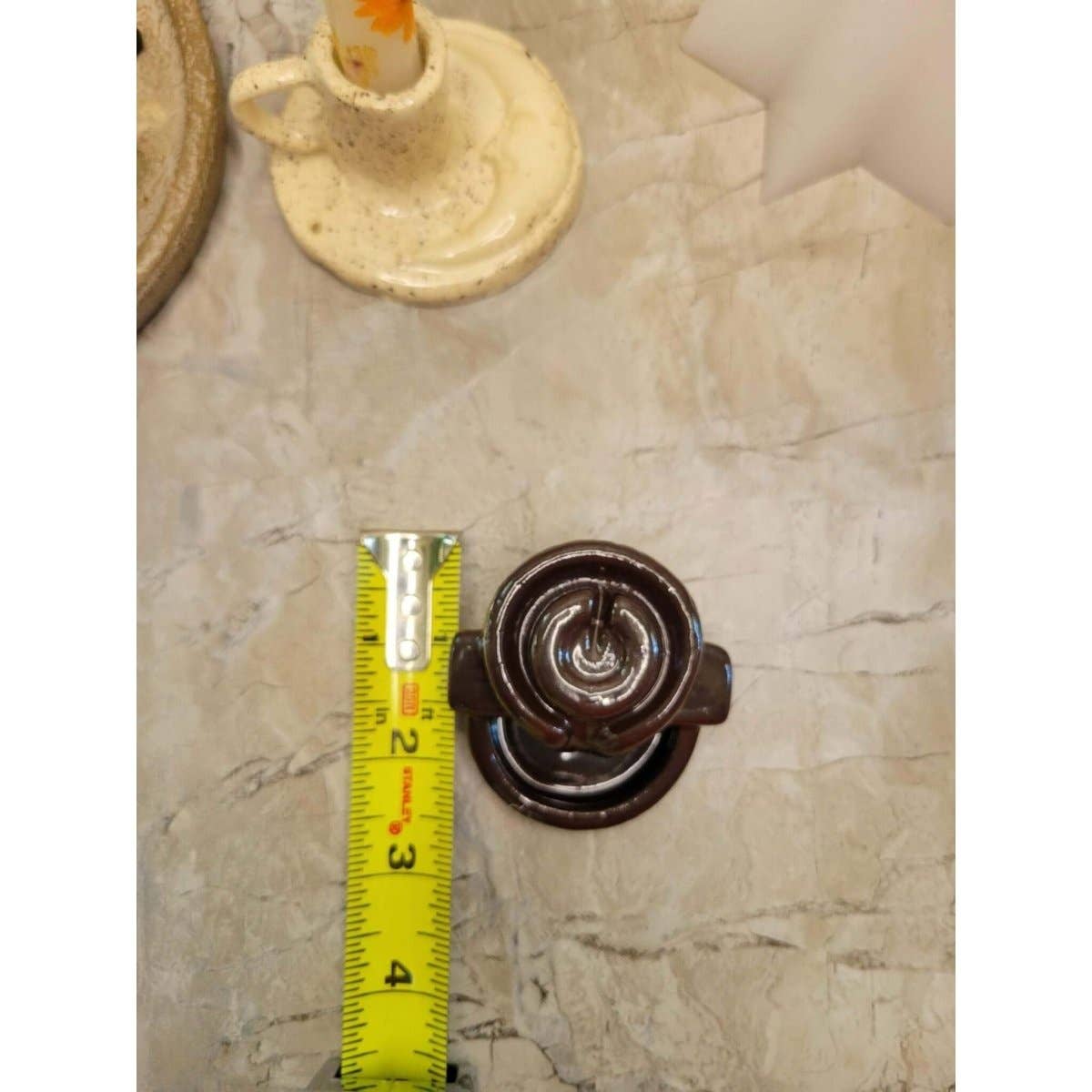 Small brown ceramic back flow incense burner next to a measuring tape on a beige tiled floor.
