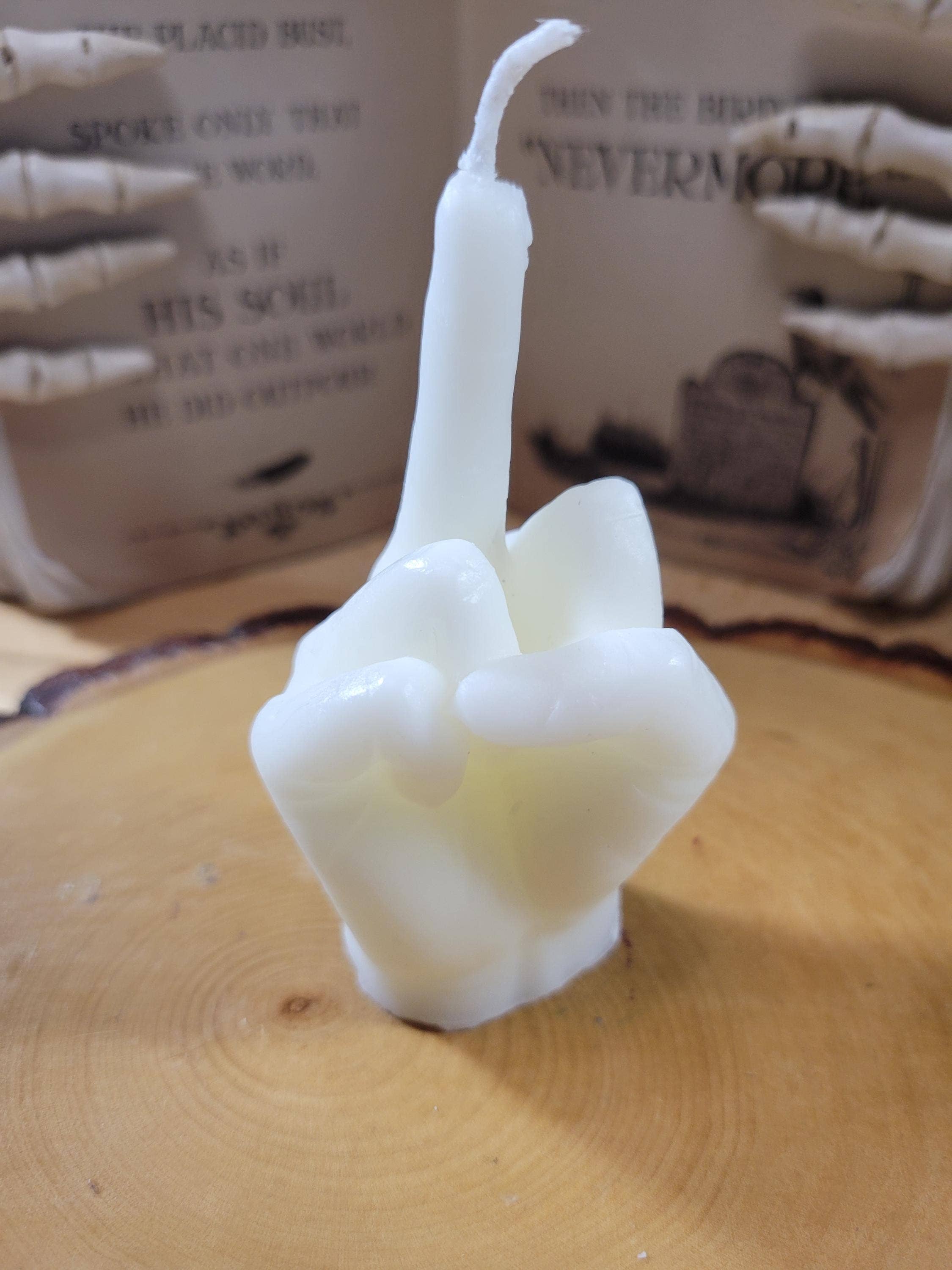 White candle shaped like a hand making a peace sign on a wooden surface with a blurred background.