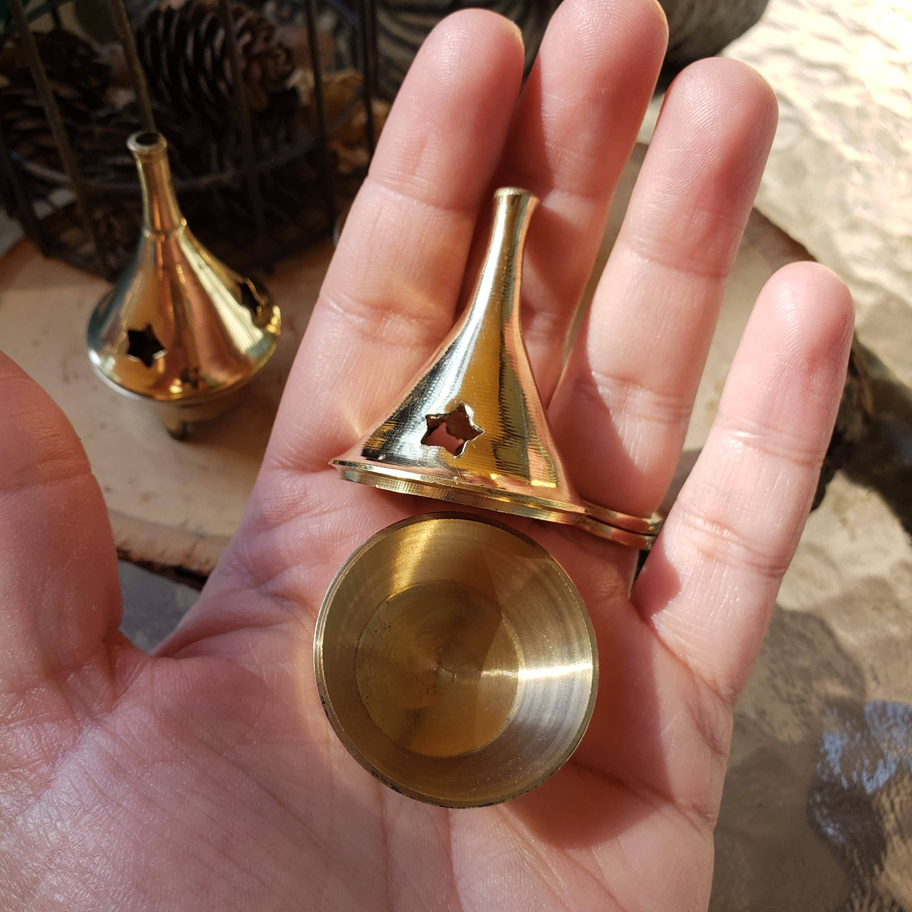 Small brass cone-shaped incense holder held in a hand with a blurred background