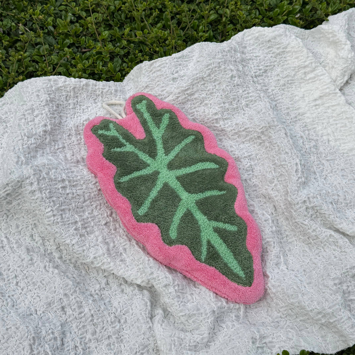 Green leaf-shaped hand towel with pink border on a textured white surface